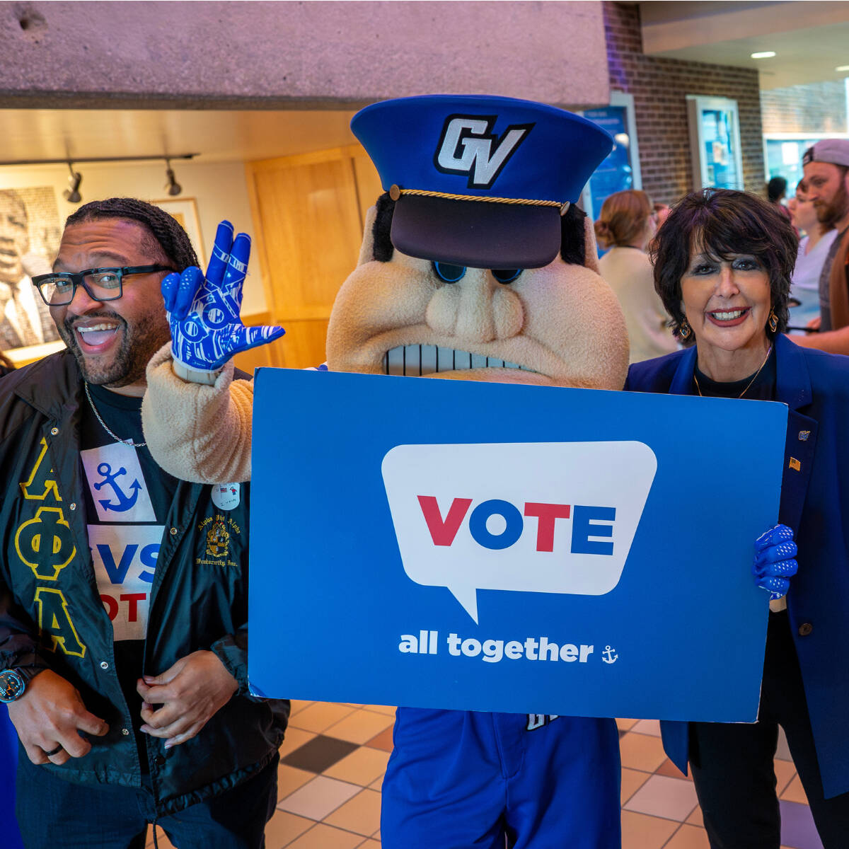 Louie the Laker holding up a sign that says "vote all together"